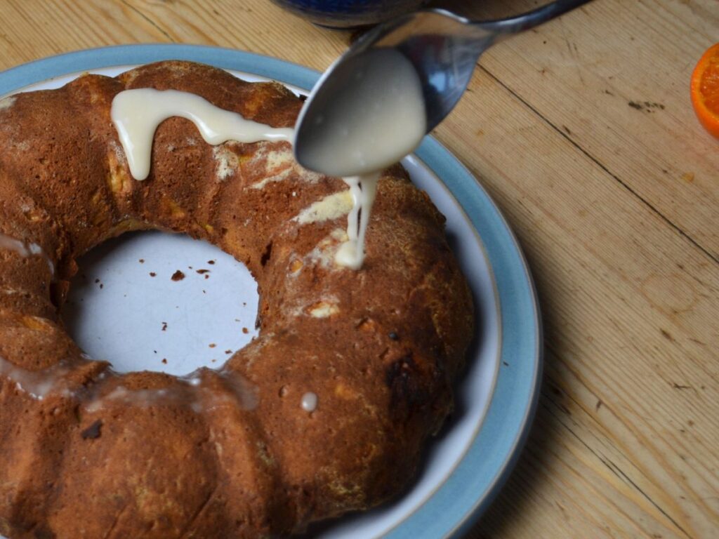 spoon pooring icing on a mandarin orange cake