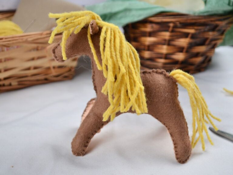 A felt horse toy o a white tablecloth with two baskets in the background