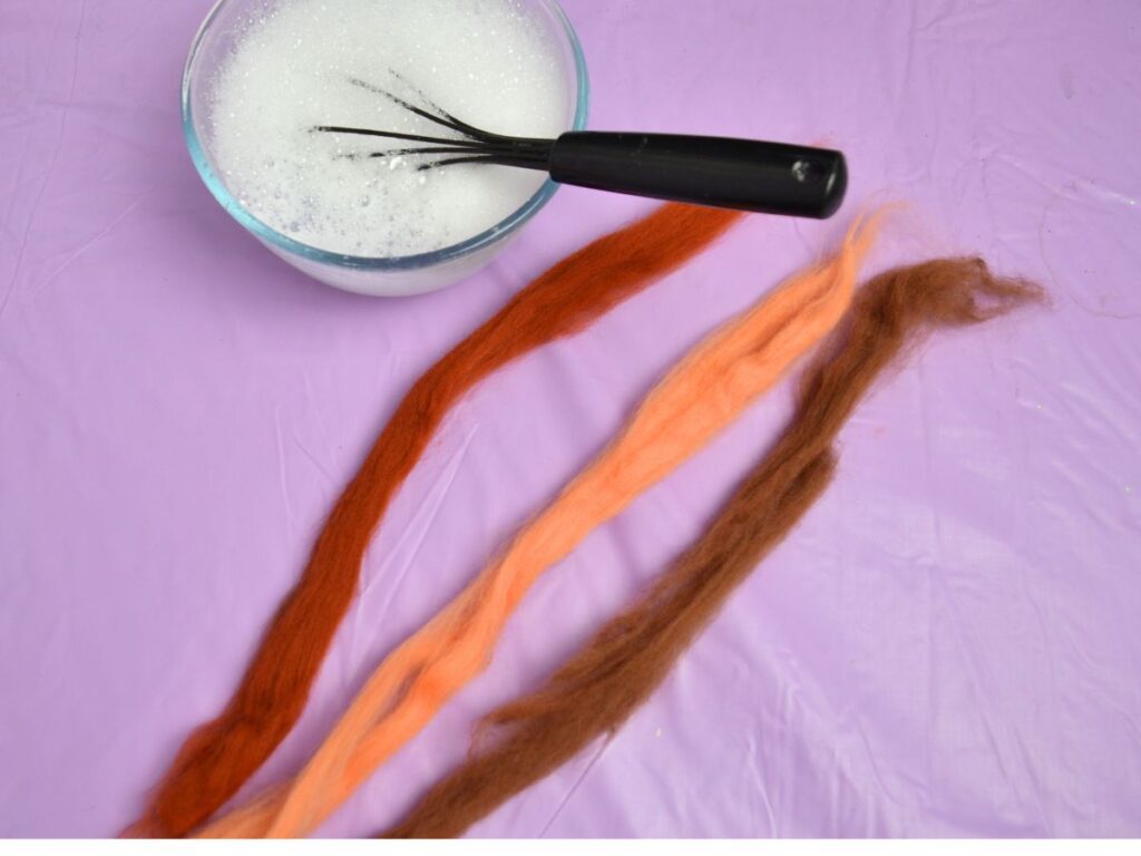 a bowl of soapy water and three long pieces of wool