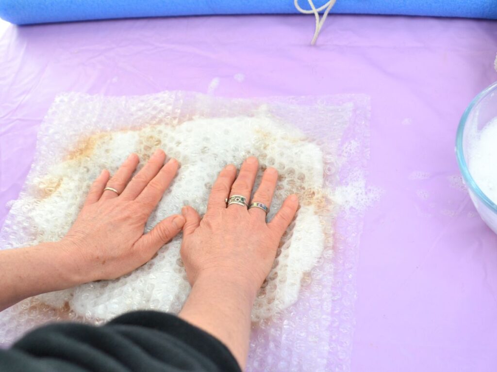 carded wool cover with soap bubbles, and bubble wrap covering it, and two hands pressing the bubble wrap