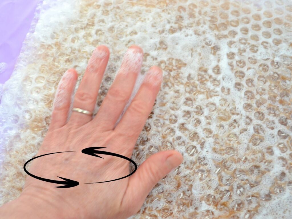 a hand on top of bubble wrap covering wet carded wool, and arrows indicating circular movements