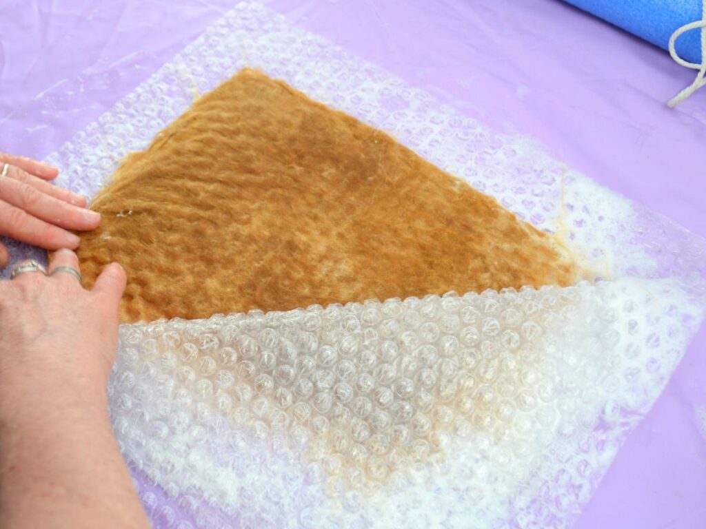 a piece of bubble wrap with wet wool on top and two hands smoothing the edges