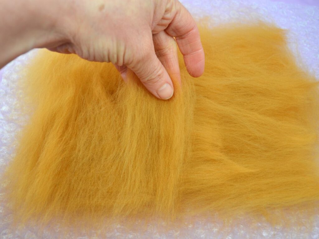 A hand laying carded wool on top of more carded wool.