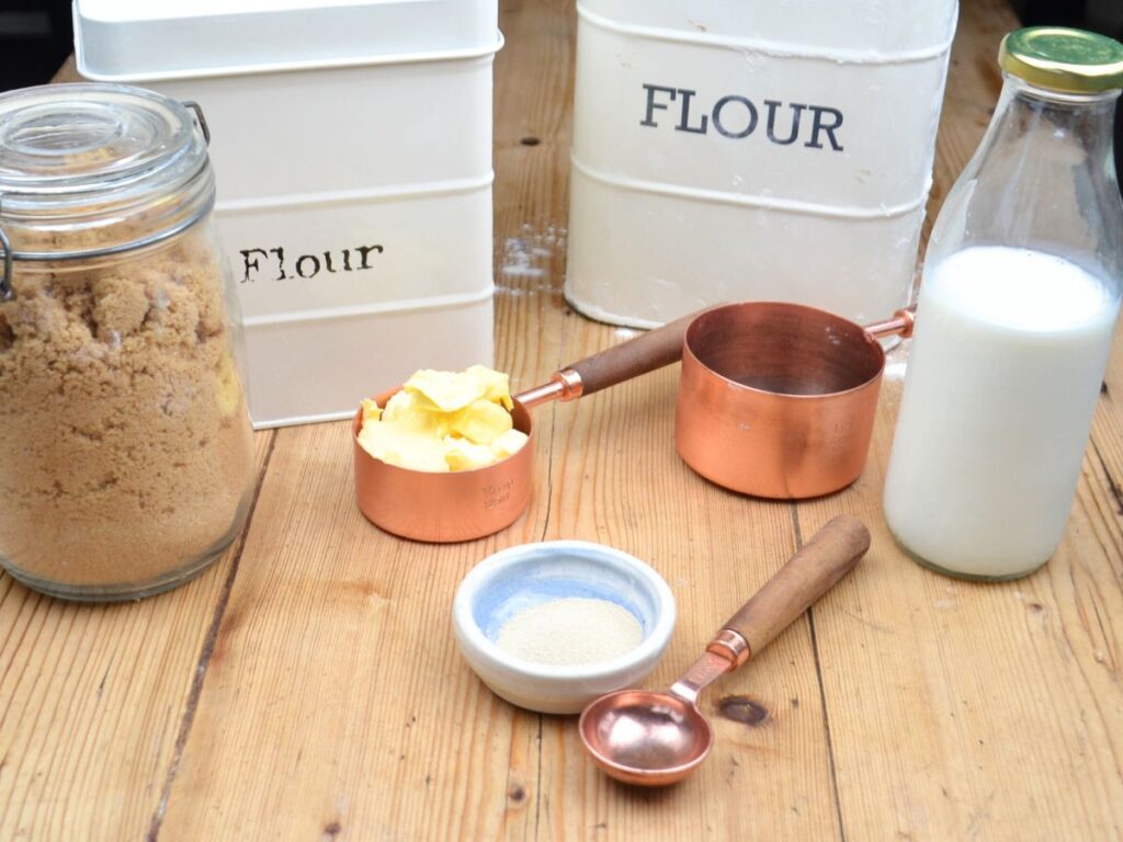 Sugar in a pot, flour in a pot, meassuring cup with butter, measuring cup, measuring spoon, a glass milk bottle.