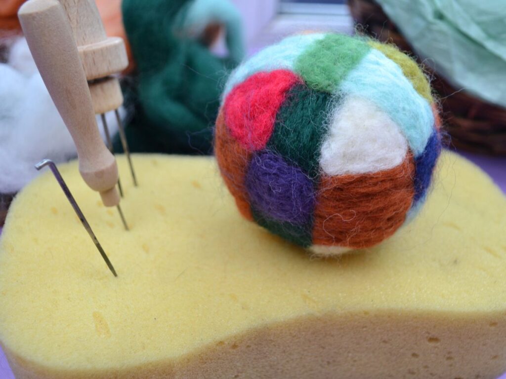 A sponge with felting needles and a finished needle felt ball.