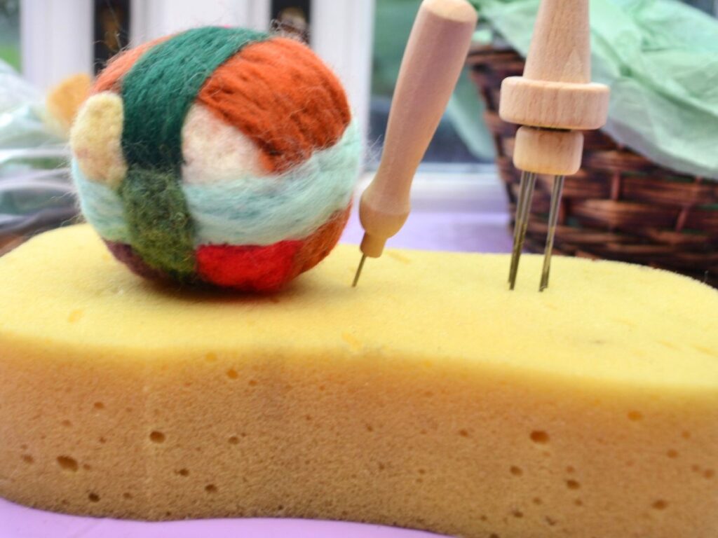 A felt ball and felting needles on a sponge