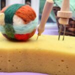 A felt ball and felting needles on a sponge