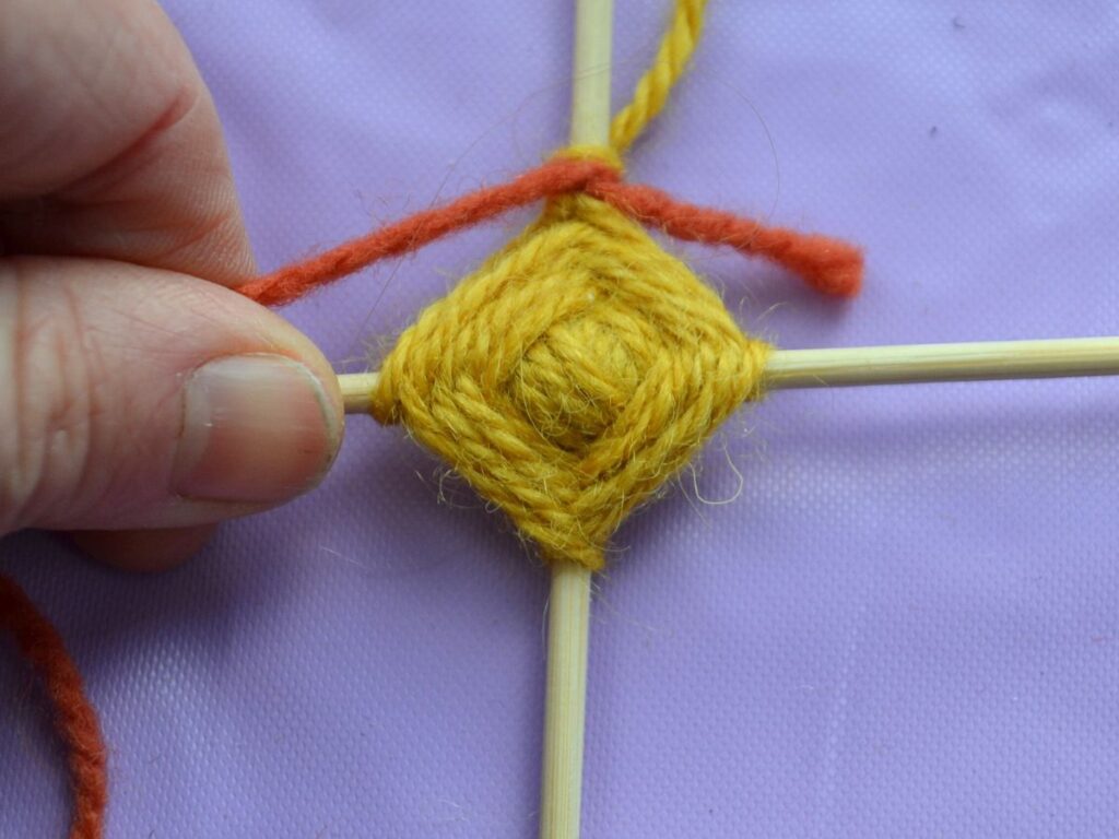 adding a new colour to the weaving of a God's eye.