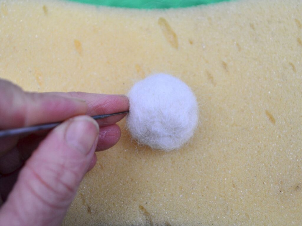  A hand poking a felt needle into a ball of wool.
