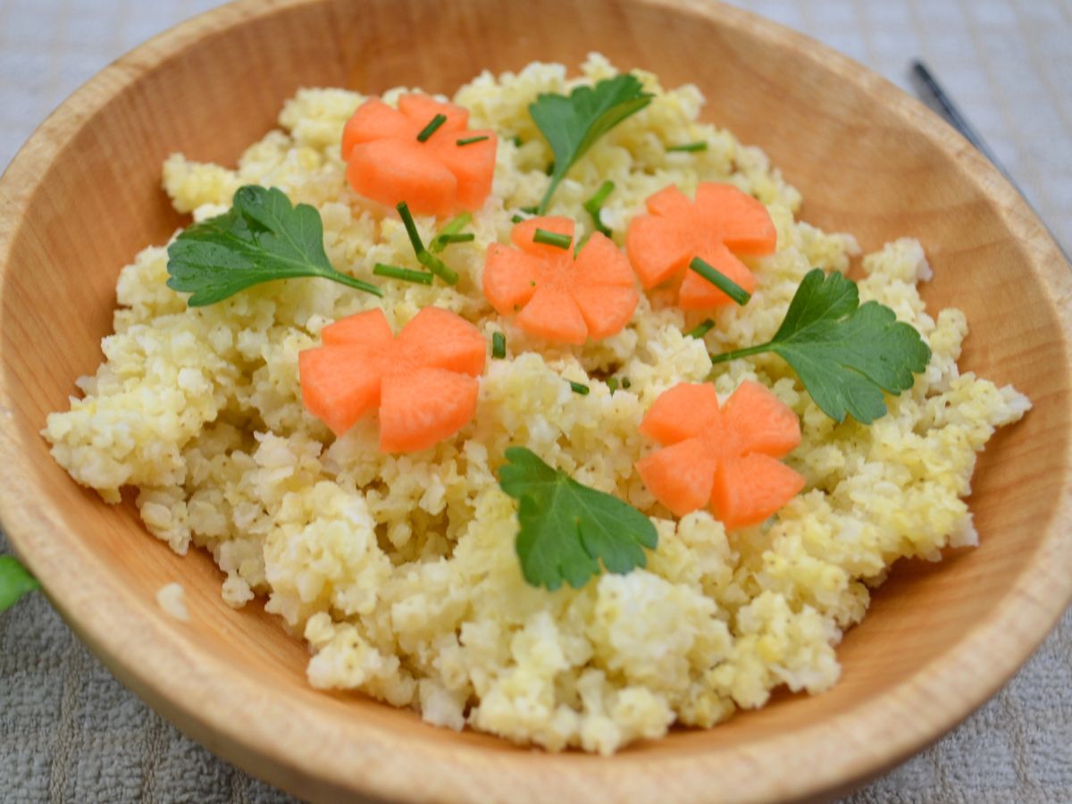 a wooden bowl with millet, carrot flowers, and parsley.