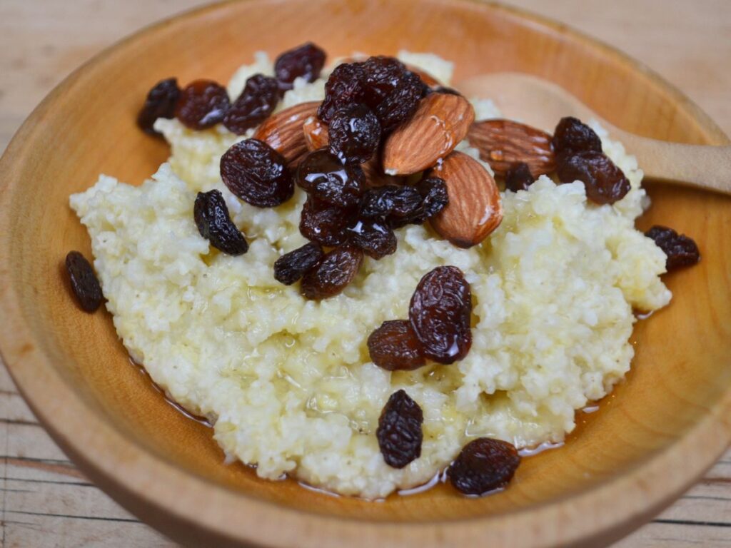 A bowl of Millet porridge, raisins, almonds, and honey.