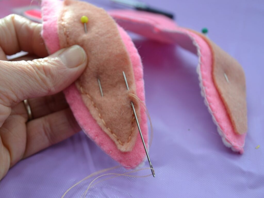 A hand sewing the inside of the ear of a Felt mask Bunny.