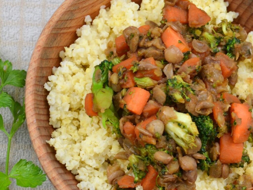 A wooden bowl with millet, vegetables and lentils.