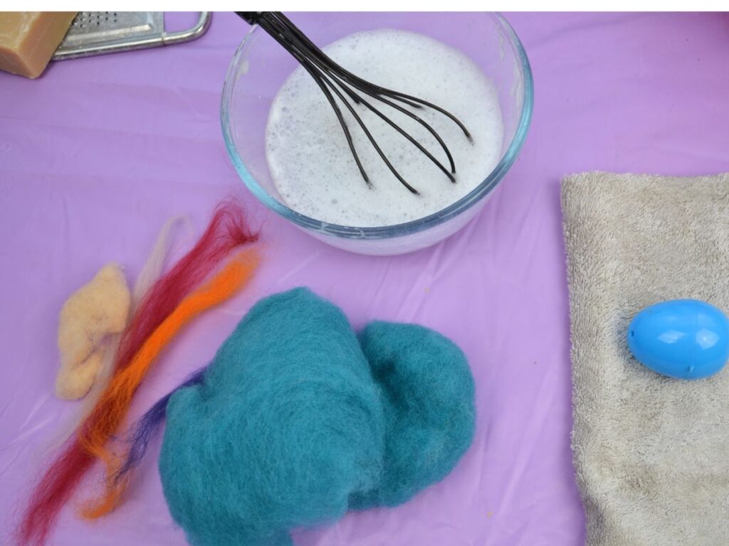 wool roving, a bowl of soapy water, a plastic egg and a towel.