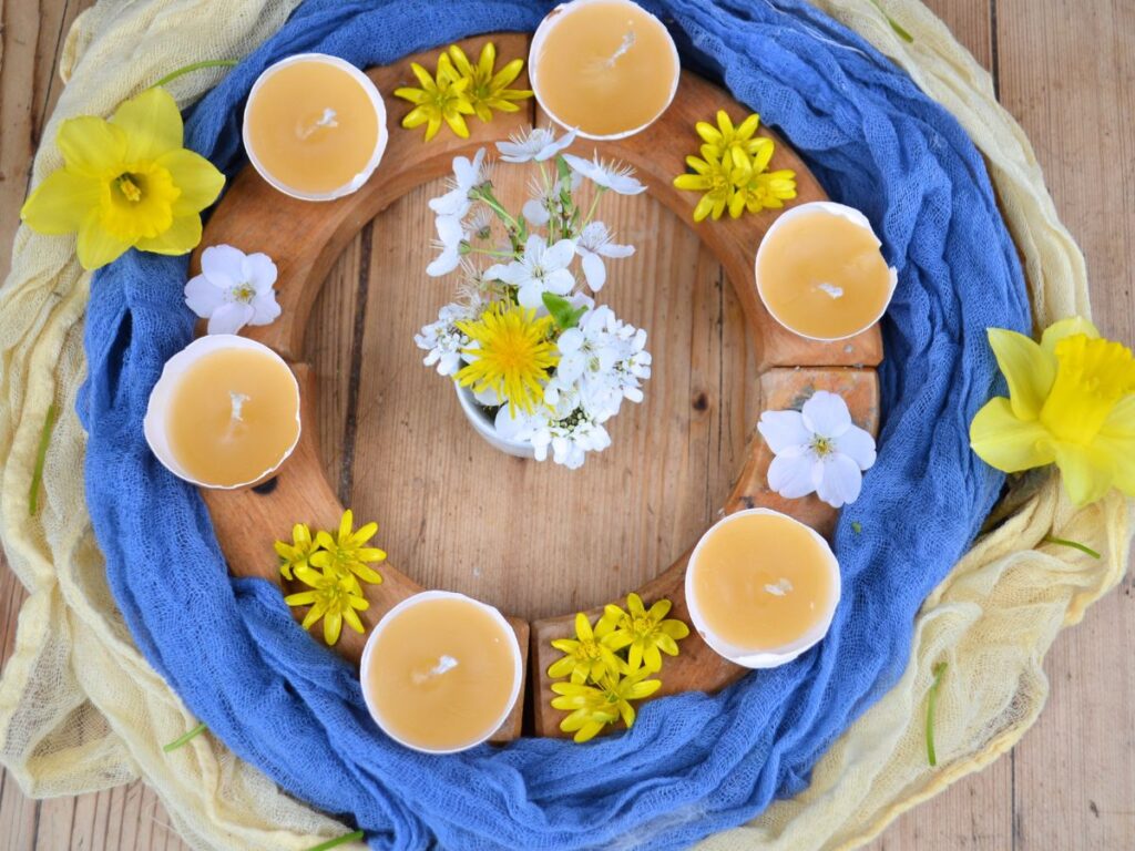 A wooden ring with flowers and eggshell candles.
