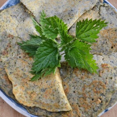 Nettle Pancakes arranged on a plate with a nettle plant in the middle.
