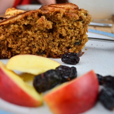 A slice of Apple Cake on a plate with apple slices and raisins.