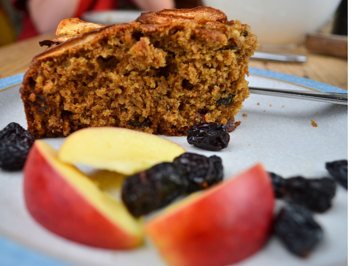 A slice of Apple Cake on a plate with apple slices and raisins.