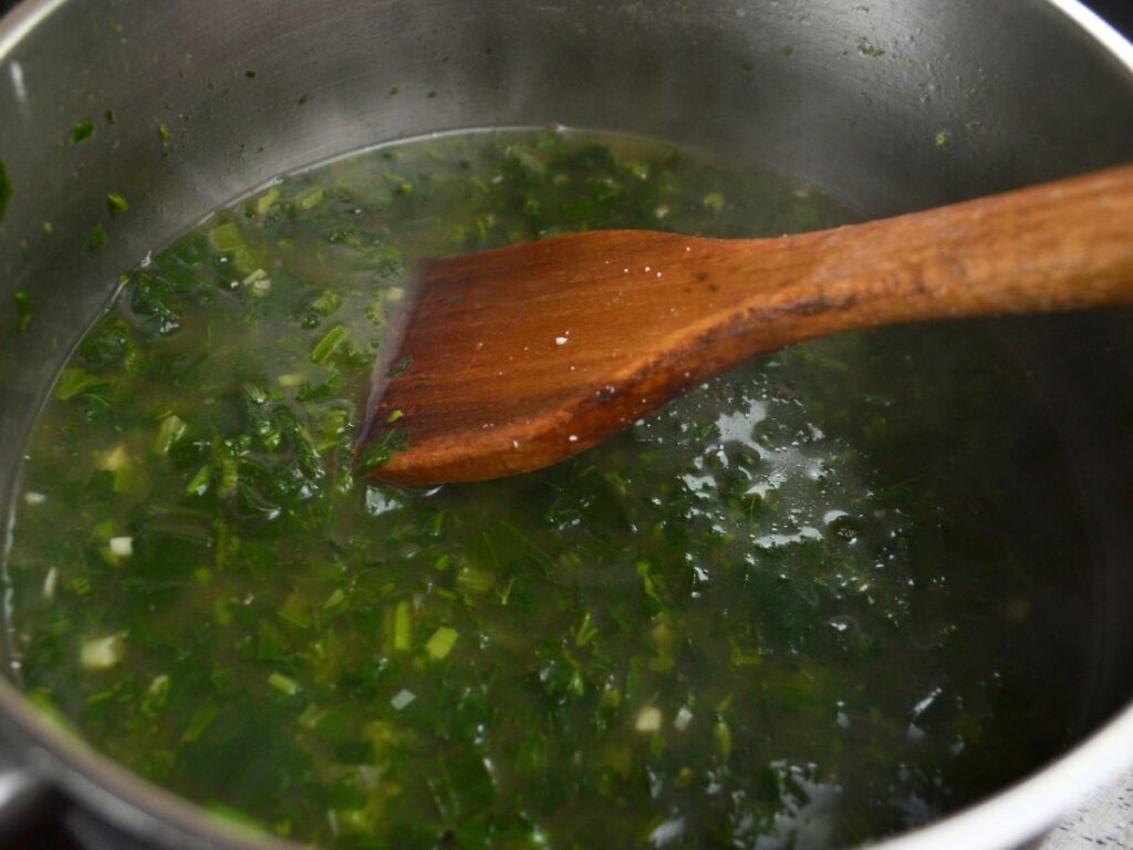 A soucepan cooking Miso Nettle Soup and a wooden spoon.