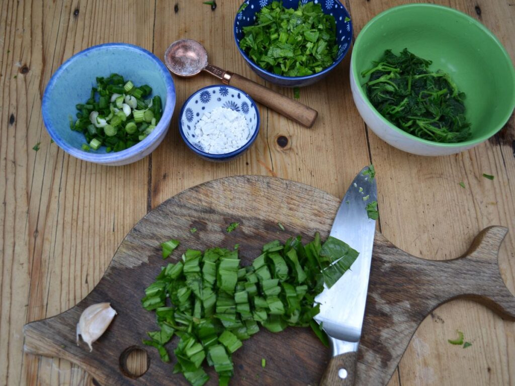A chopping board with chopped wild garlic, and little bowls with chopped vegetables, and kudzu.
