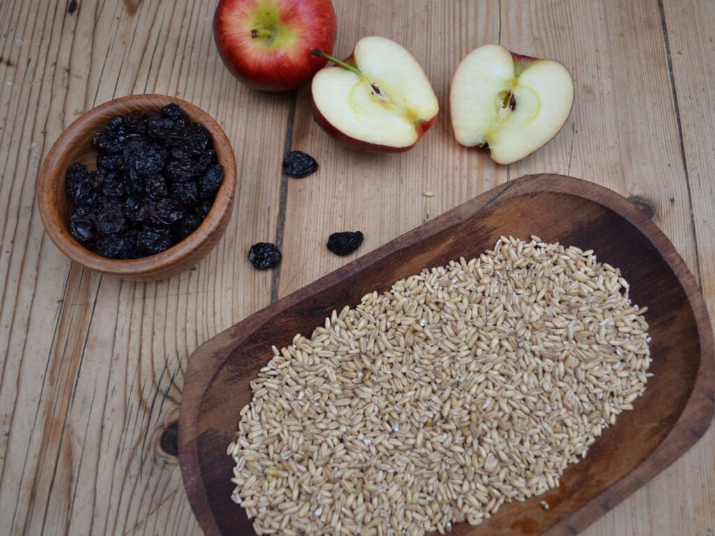 A little wooden bowl with raisins, apples and a wooden plate with oat groats.