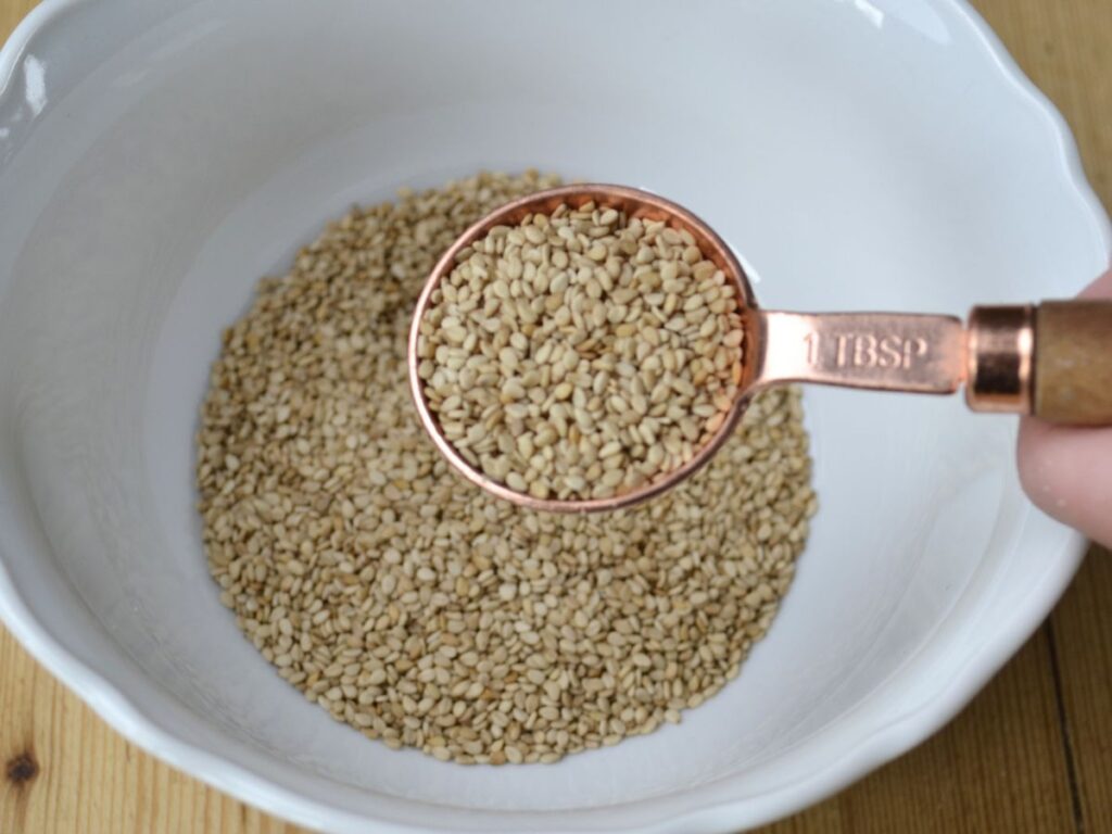 Sesame seeds in a bowl and a measuring spoon.