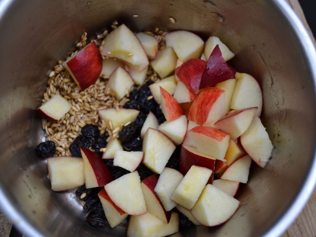 A saucepan with oat groats, apples and raisins.