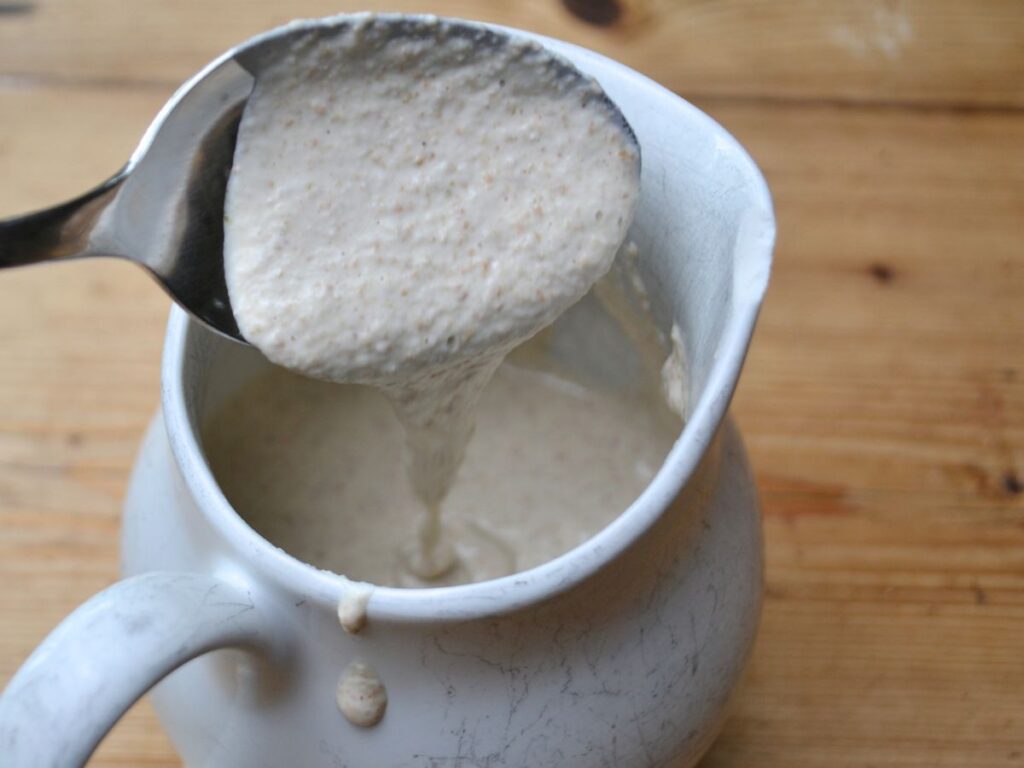 A spoon pouring Buckwheat crêpes batter into a jug.