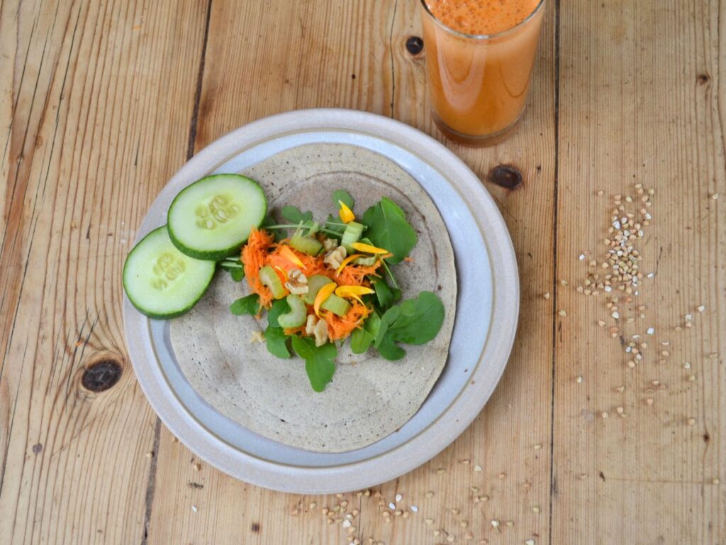 A buckwheat crêpe on a plate with a salad on top, and a glass of juice.