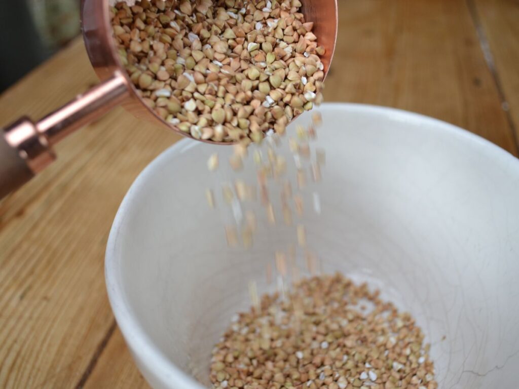 Pouring buckwheat with a measuring cup into a bowl.
