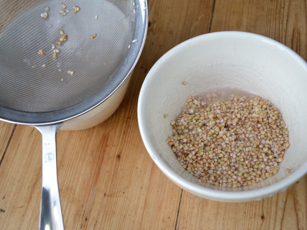 Buckwheat in a bowl, another bowl with a sieve on top.