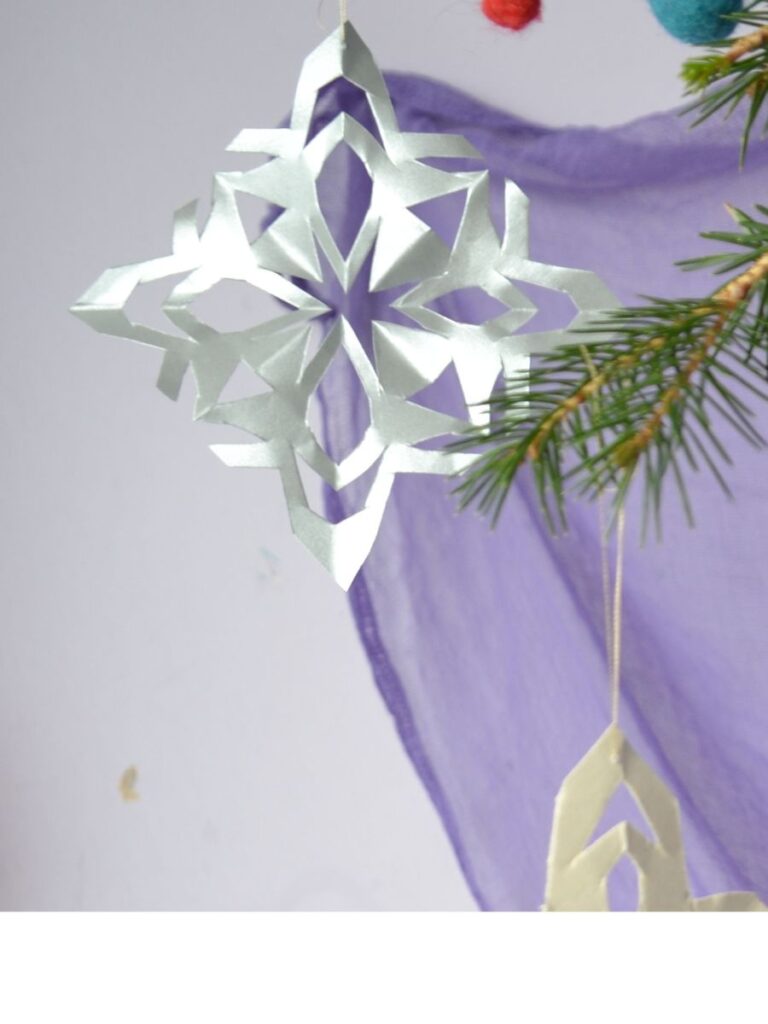 A paper snowflake hanging from a Christmas tree.